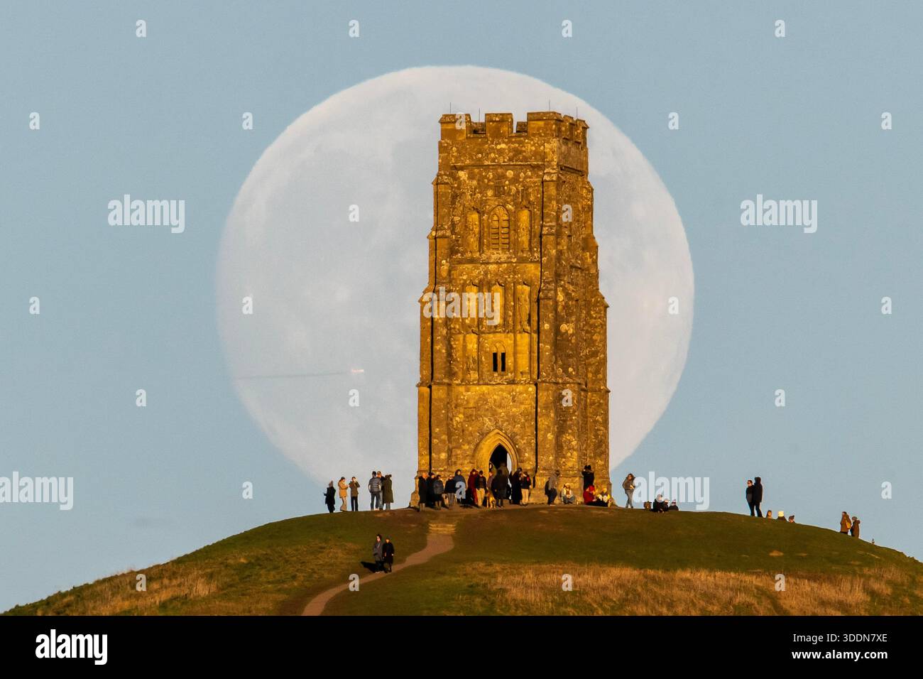 Glastonbury, Somerset, Royaume-Uni. 2 janvier 2026. Météo britannique. La lune presque pleine Wolf Moon se lève dans le ciel clair de l'après-midi de derrière la tour St Michael sur Glastonbury Tor à Glastonbury dans le Somerset comme une grande foule regarde. Ce mois la pleine lune est le 3 janvier sera une super lune. Crédit photo : Graham Hunt/Alamy Live News Banque D'Images