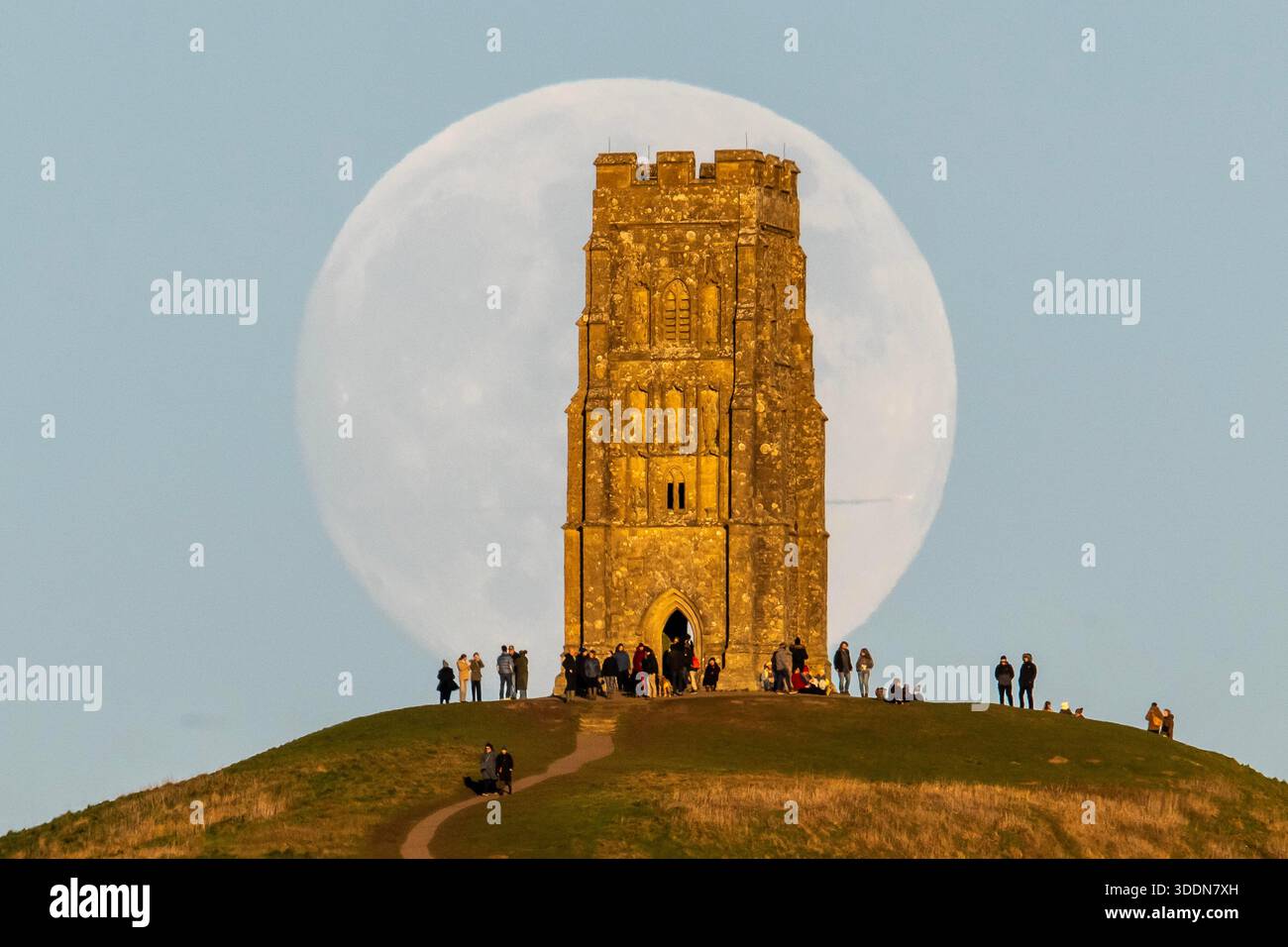 Glastonbury, Somerset, Royaume-Uni. 2 janvier 2026. Météo britannique. La lune presque pleine Wolf Moon se lève dans le ciel clair de l'après-midi de derrière la tour St Michael sur Glastonbury Tor à Glastonbury dans le Somerset comme une grande foule regarde. Ce mois la pleine lune est le 3 janvier sera une super lune. Crédit photo : Graham Hunt/Alamy Live News Banque D'Images