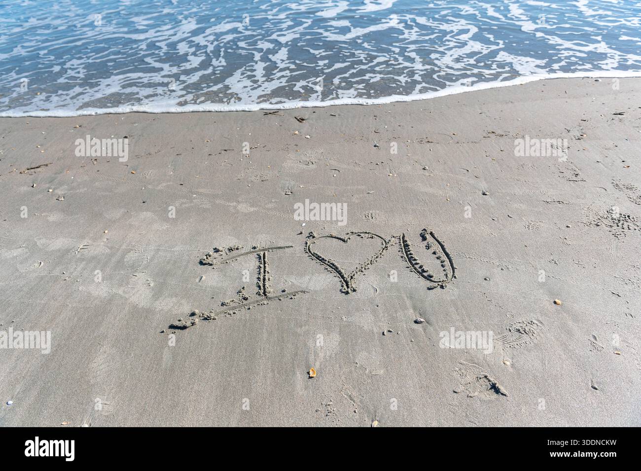 Une plage avec un cœur écrit dans le sable. Le cœur est entouré de rochers et le sable est mouillé. Concept d'amour et de chaleur, comme si quelqu'un avait laissé un M. Banque D'Images