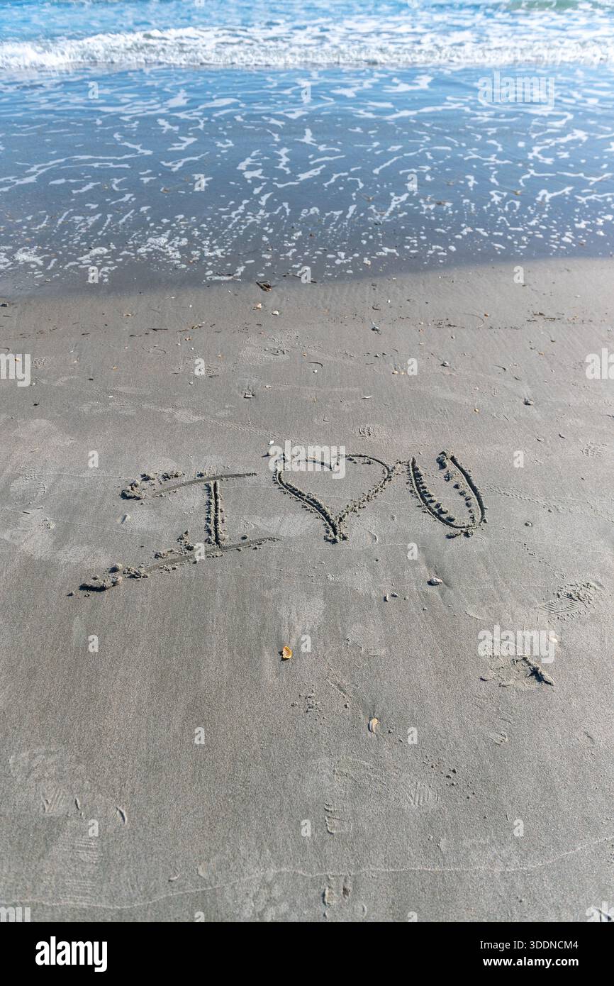 Une plage avec un cœur écrit dans le sable. Le cœur est entouré de rochers et le sable est mouillé. Concept d'amour et de chaleur, comme si quelqu'un avait laissé un M. Banque D'Images