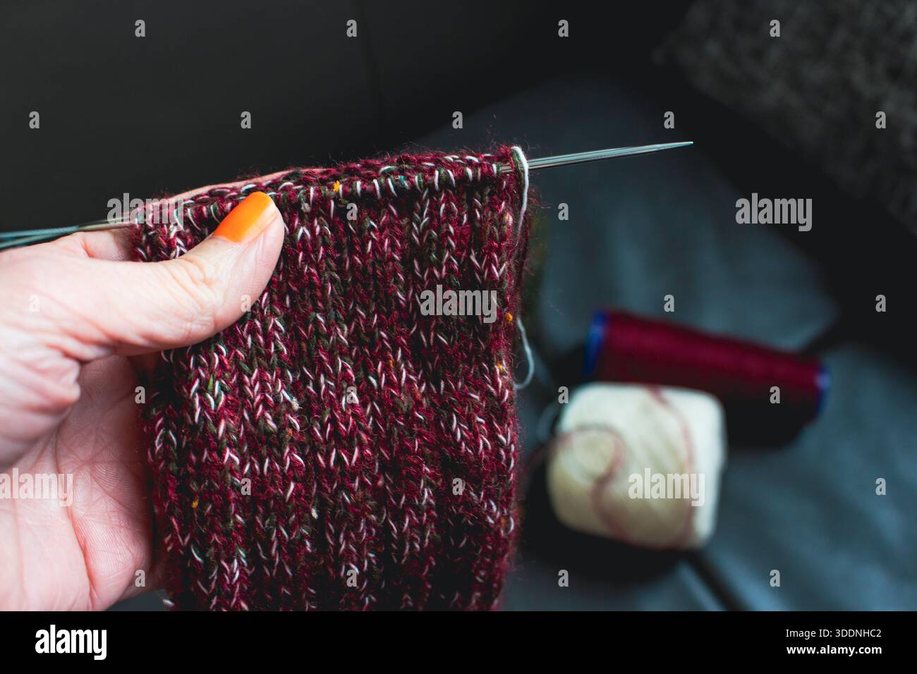 Femme tenant des chaussettes tricotées confortables sur des aiguilles à la main. Mélange de fils rouges, verts et blancs sur aiguilles à tricoter. Procédé de tricotage de chaussettes en laine. Banque D'Images