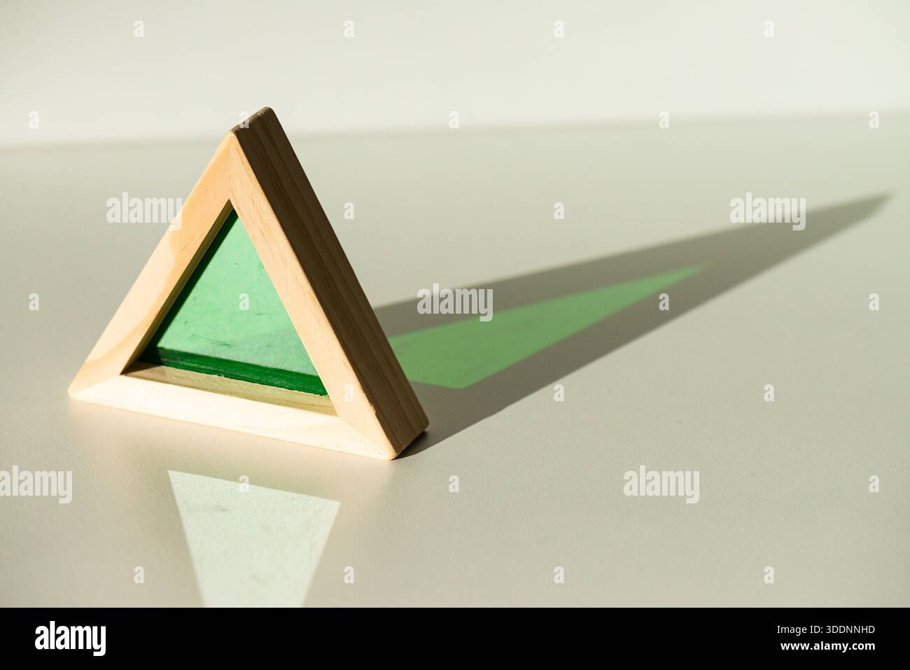 Un triangle équilatéral en bois, avec un milieu transparent vert, projetant une ombre d'un triangle isocèle Banque D'Images