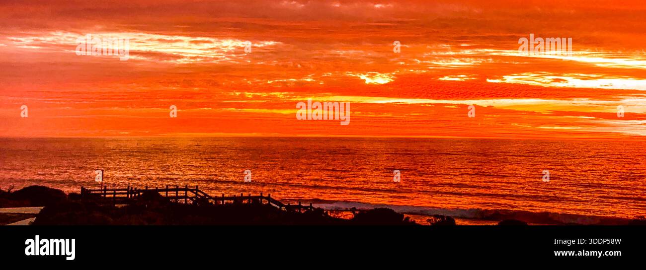 Un coucher de soleil spectaculaire présente des teintes orange et rouge vibrantes dans le ciel, illuminant les nuages sur l'océan serein. Banque D'Images