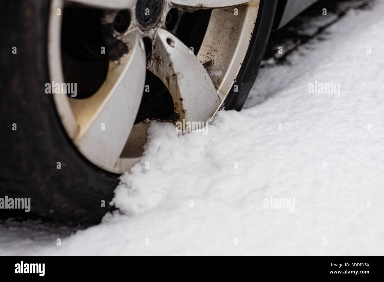 Une voiture est coincée dans la neige, avec sa roue partiellement encastrée dans un monticule de neige blanche. La scène montre les défis des conditions de conduite hivernales. Banque D'Images