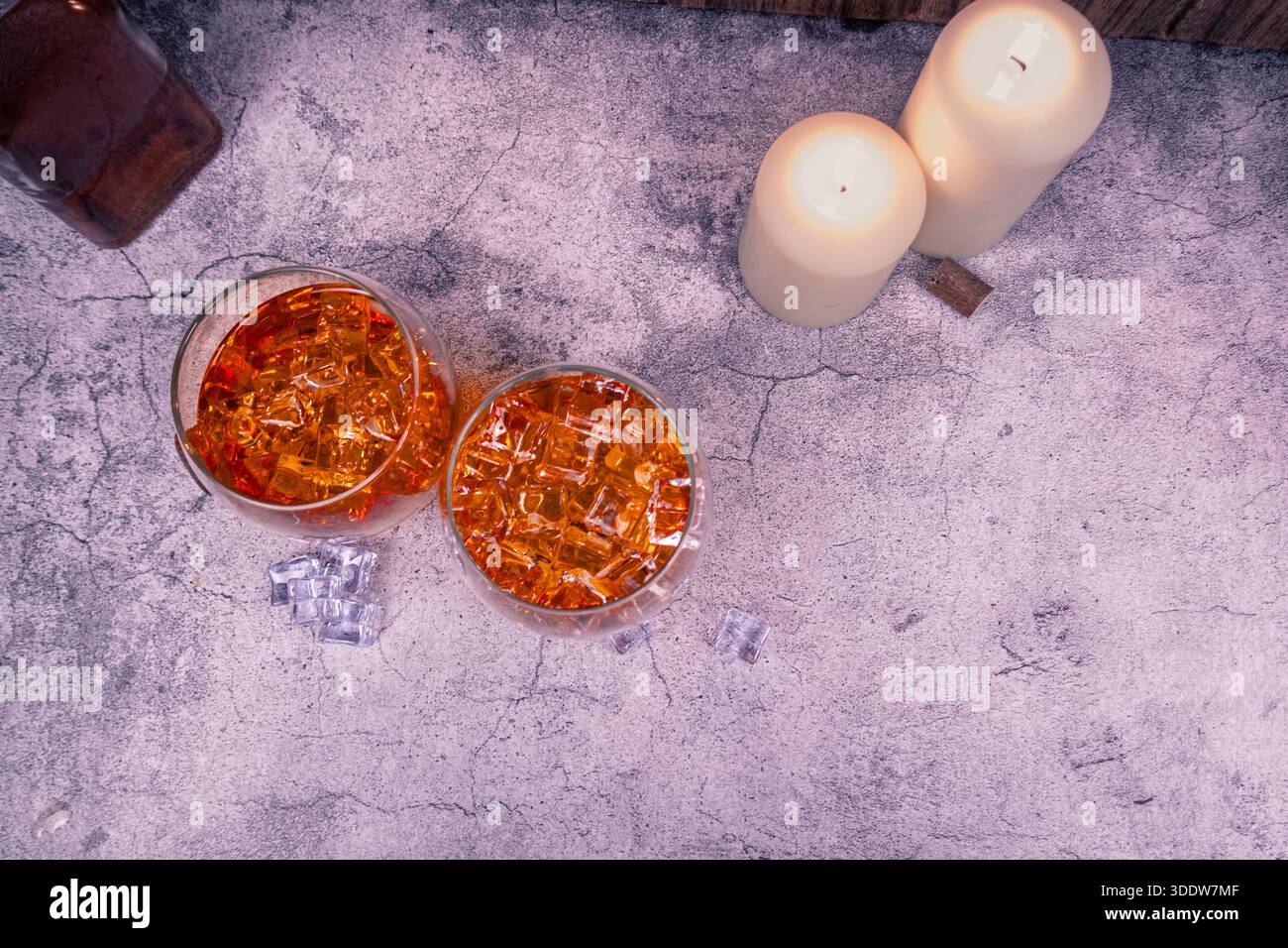 Vue aérienne de deux boissons de whisky avec de la glace sur la texture de béton fissuré, des bougies dans un coin et beaucoup d'espace de copie. Pose à plat minimale de la barre. Banque D'Images