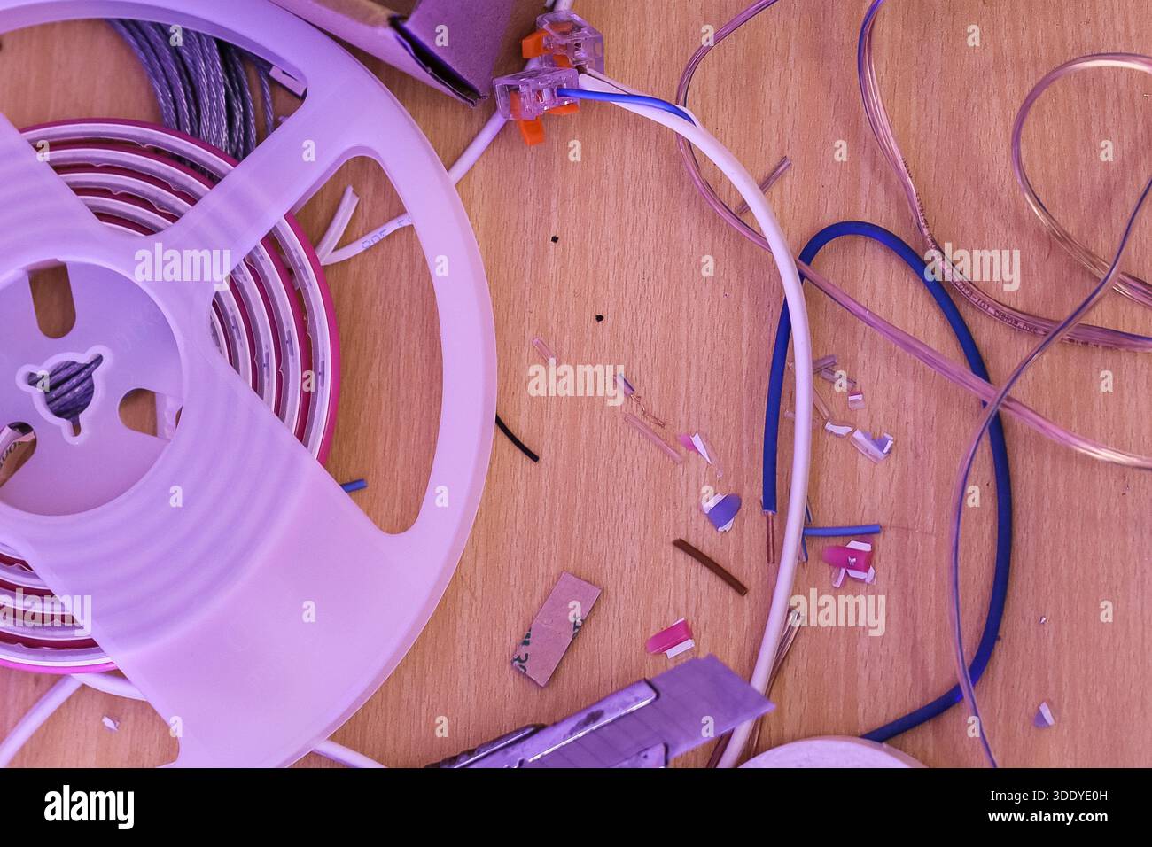 Gros plan de bandes lumineuses à LED enroulées, de câbles et de débris disposés de manière messily sur une surface en bois à l'intérieur Banque D'Images