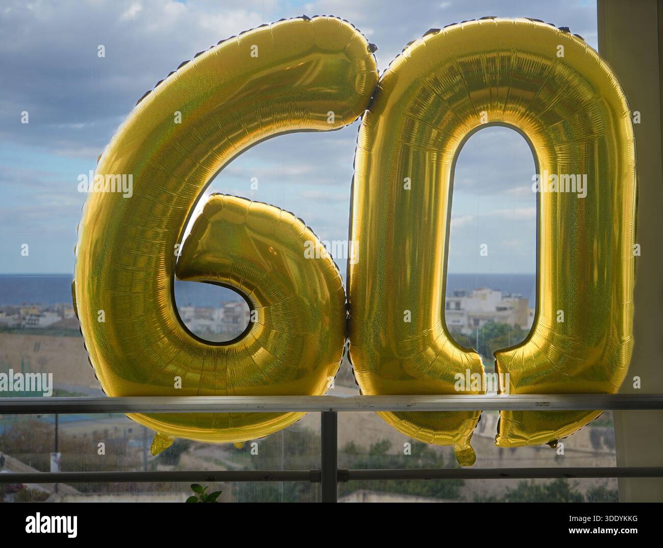 De grandes feuilles d'or numéro 60 ballons célébrant un 60e anniversaire. Décorations festives placées sur un balcon avec vue sur la ville et la mer. Banque D'Images