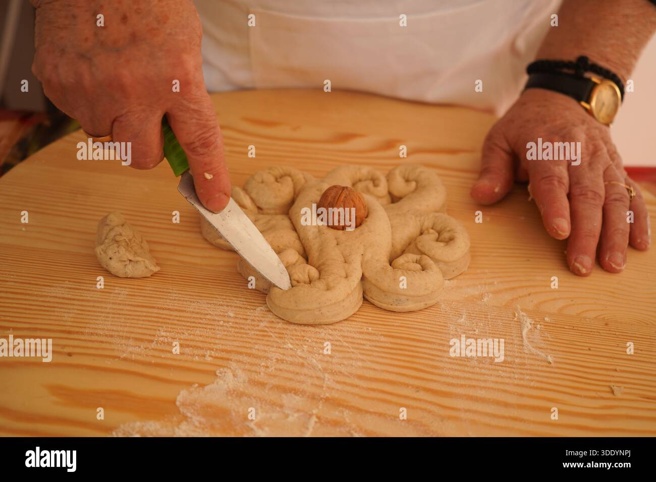 Les mains de grand-mère utilisant un couteau pour façonner la pâte traditionnelle Christopsomo en un motif de grenouille 'afordakos' avec une noix. Authentique patrimoine culinaire grec. Banque D'Images