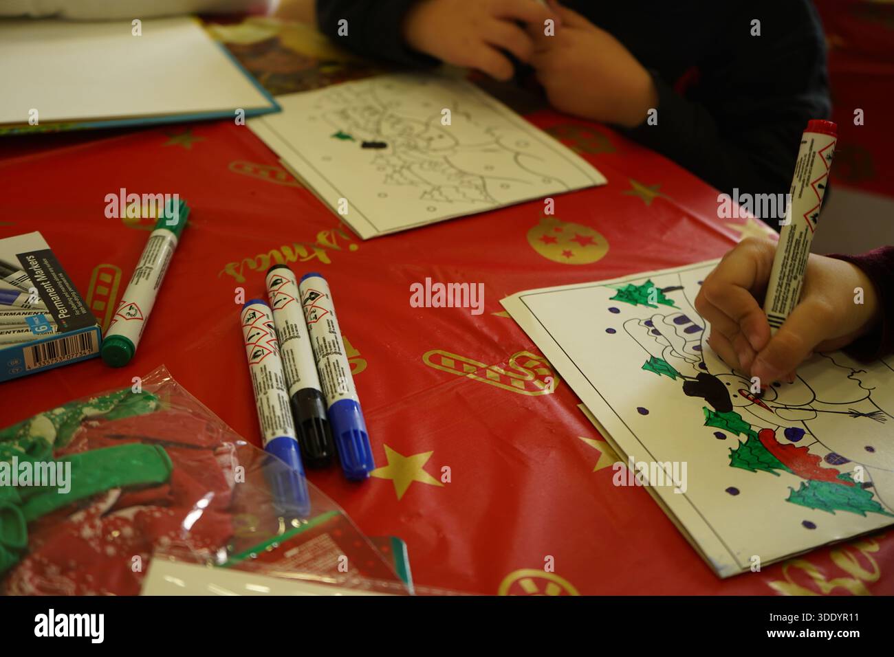 Plan en grand angle d'enfants coloriant des dessins festifs sur une nappe rouge de Noël avec des marqueurs et des ballons. Ambiance chaleureuse et authentique des activités de vacances Banque D'Images