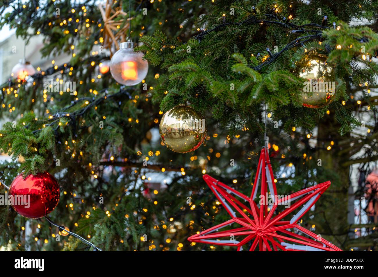 Gros plan sur les décorations de sapin de noël avec des boules rouges et dorées, des ornements en forme d'étoile et des lumières chaudes imitant le feu, ambiance festive de vacances Banque D'Images