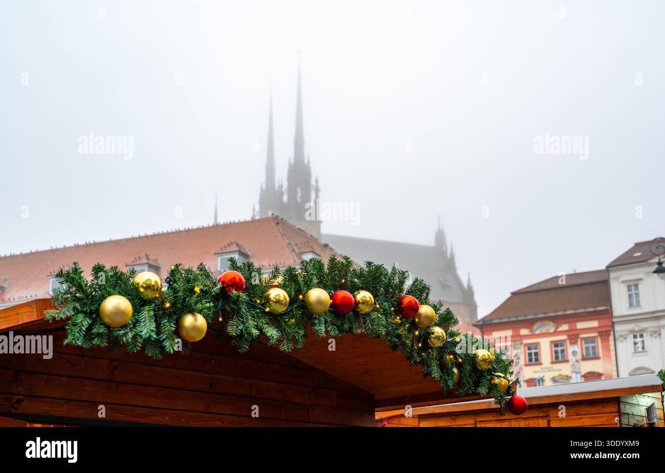 Toit décoré d'un étal de marché de noël avec des branches de sapin et des ornements rouges et dorés, atmosphère de ville de brno avec silhouette brumeuse de pierre et paul Banque D'Images
