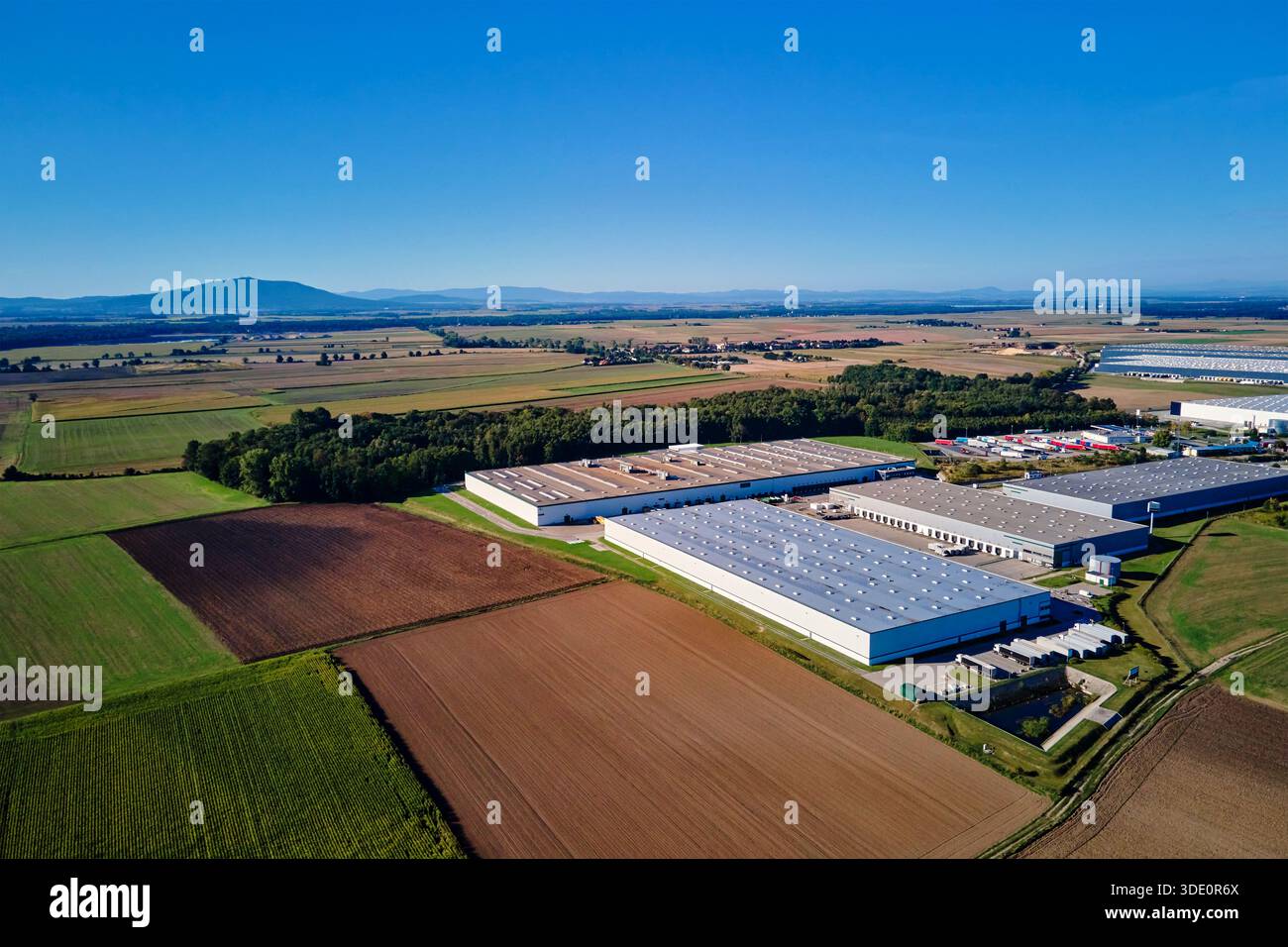 Vue aérienne du grand complexe d'entrepôt industriel et centre logistique dans la zone rurale avec des champs et des montagnes en arrière-plan Banque D'Images