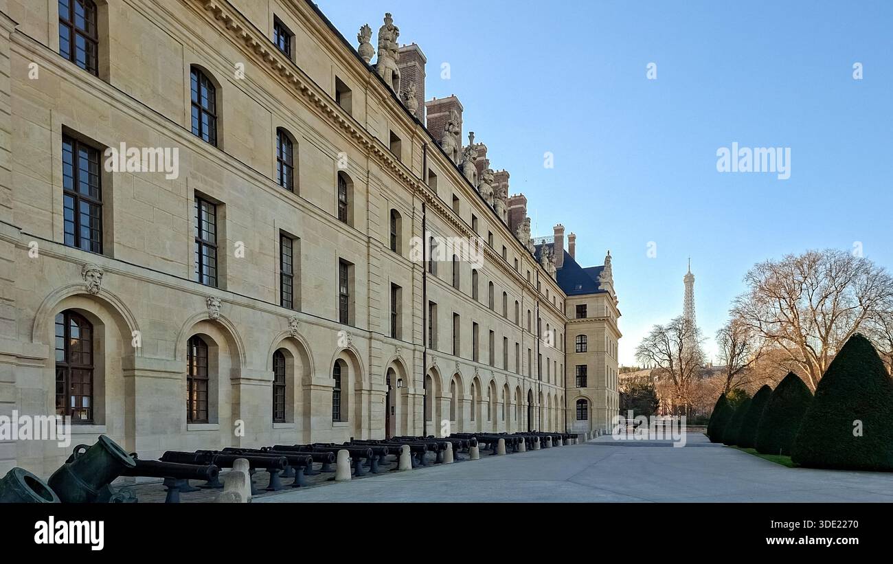 Deux adultes traversent une cour historique près d'un grand bâtiment à Paris. La Tour Eiffel se dresse en arrière-plan sous un ciel dégagé. Cette sp Banque D'Images