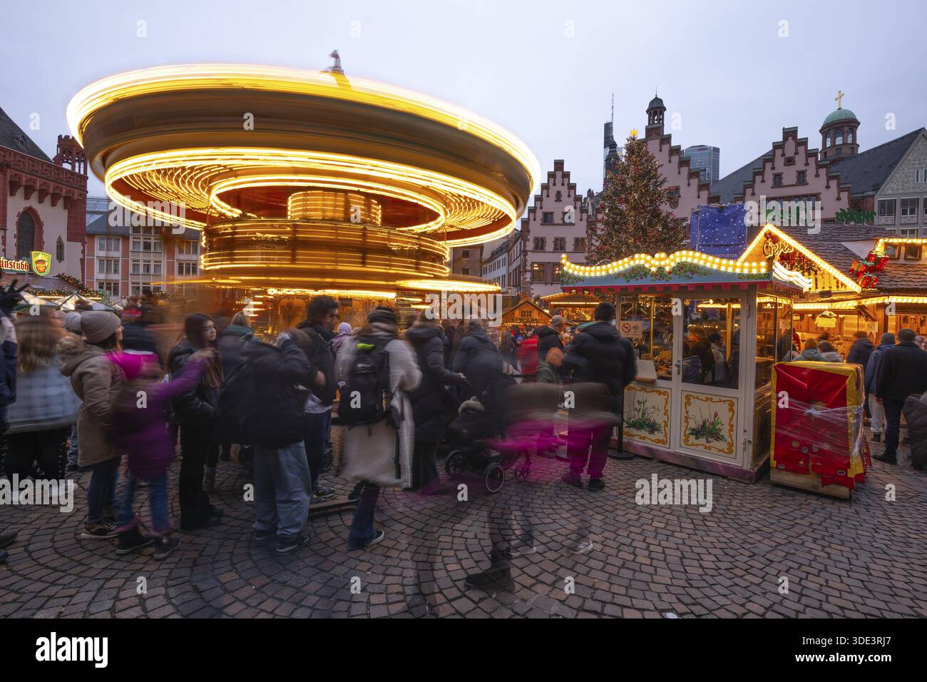 22 décembre 2025, marché de Noël de Francfort sur Roemerberg avec la ligne d'horizon en arrière-plan au crépuscule. Les lumières brillent et les enfants sont carous Banque D'Images