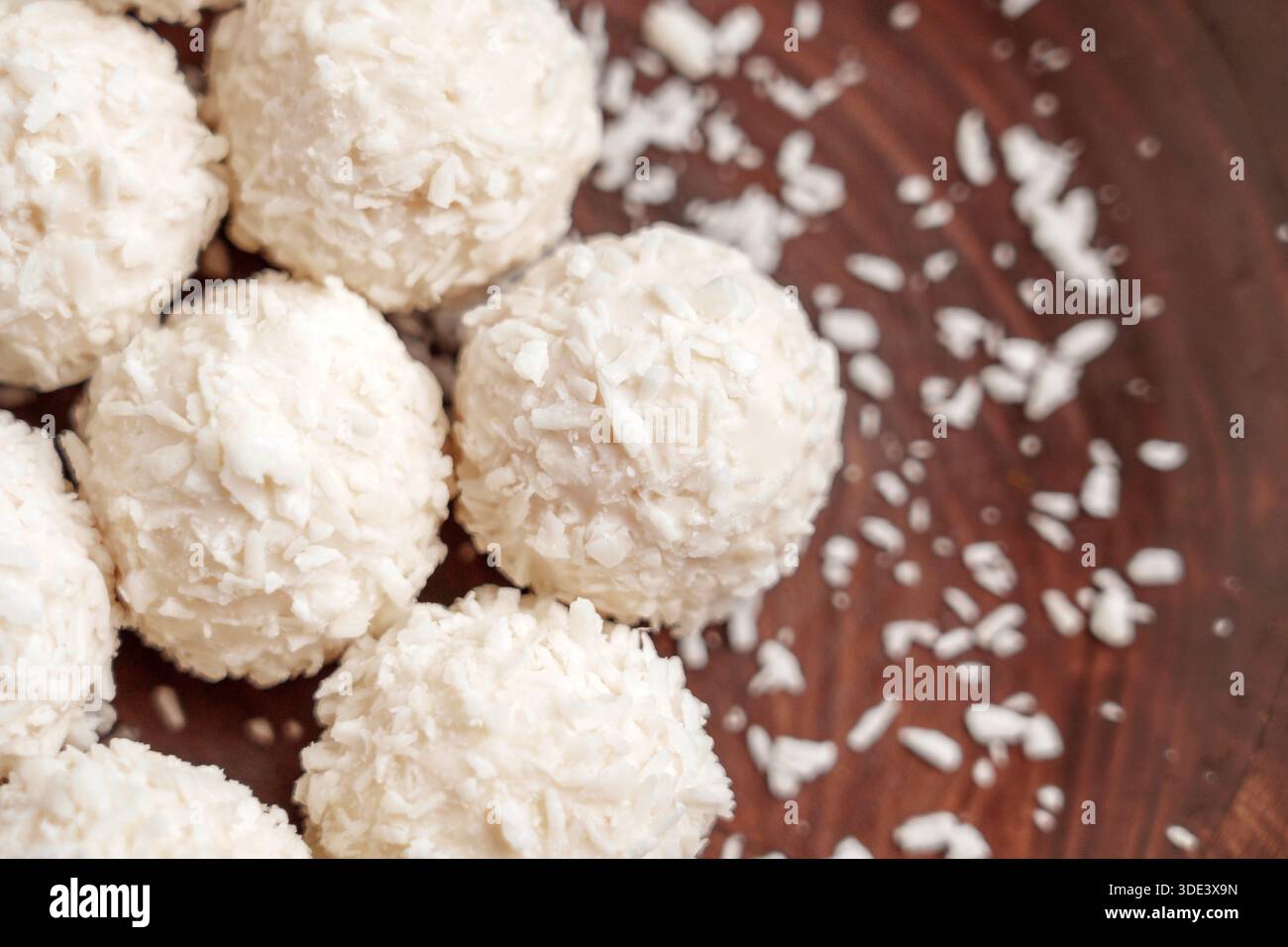 Bonbons sphériques doux enduits de flocons de noix de coco sur une surface en bois foncé Banque D'Images