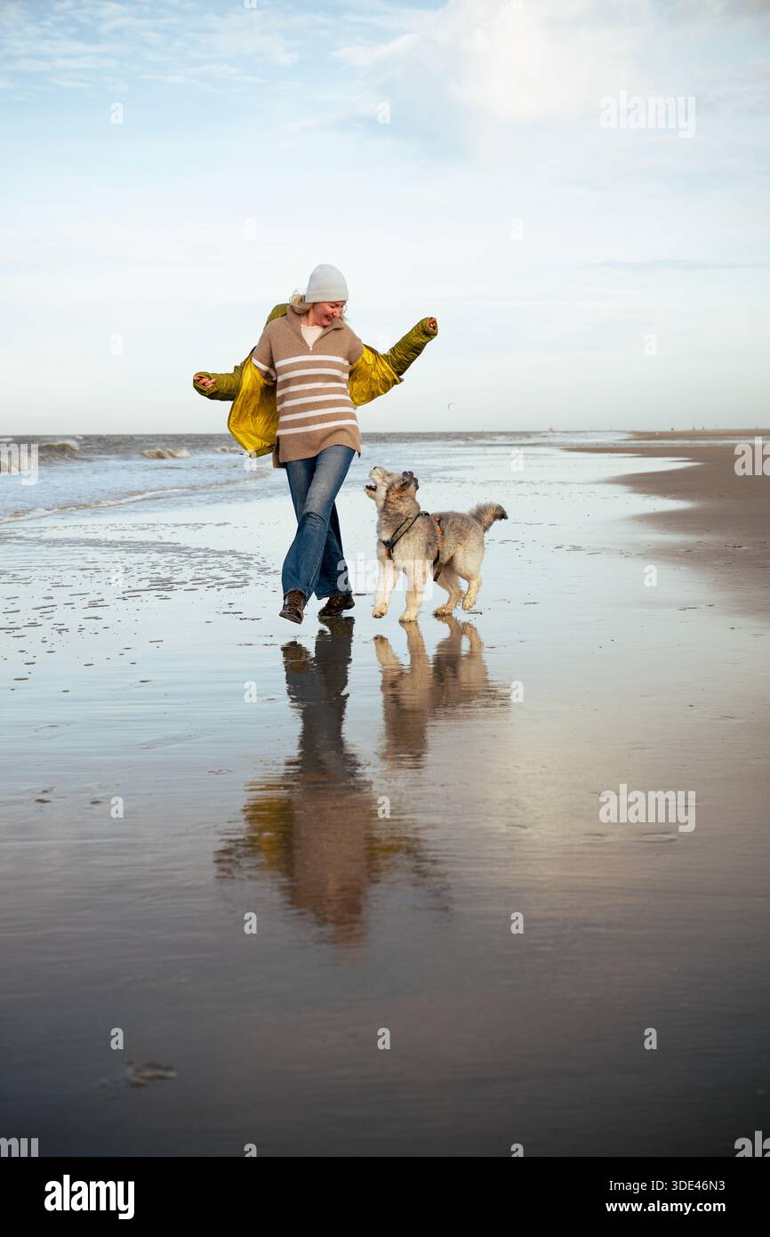 Femme courant avec un chien sur la plage vide de la mer du Nord pendant la promenade joyeuse Banque D'Images