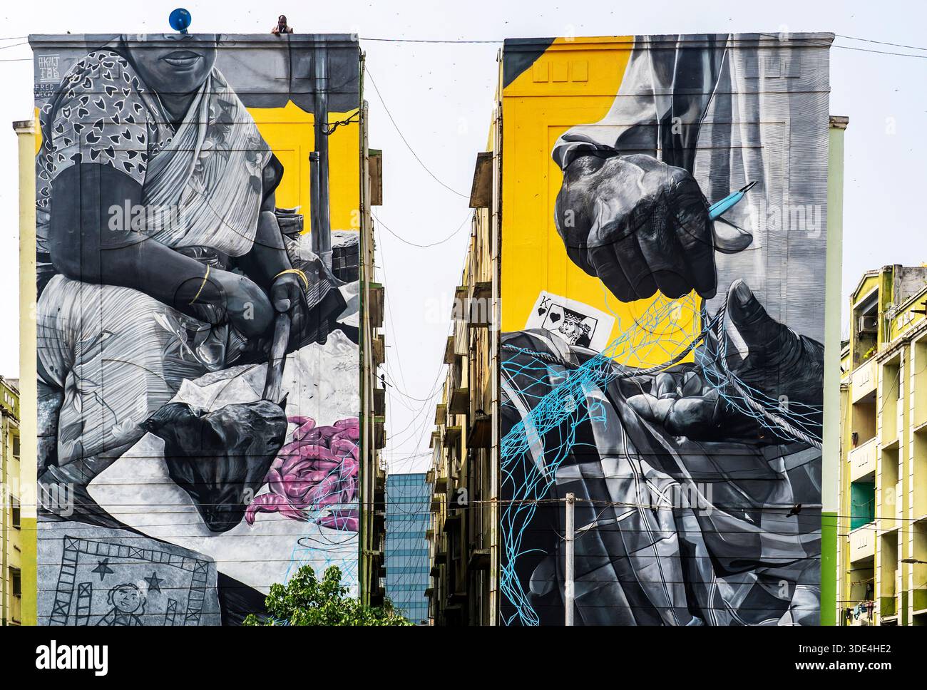 Grandes peintures murales en noir et blanc sur deux bâtiments adjacents représentant des mains et une femme en tenue traditionnelle, avec des accents colorés. Banque D'Images