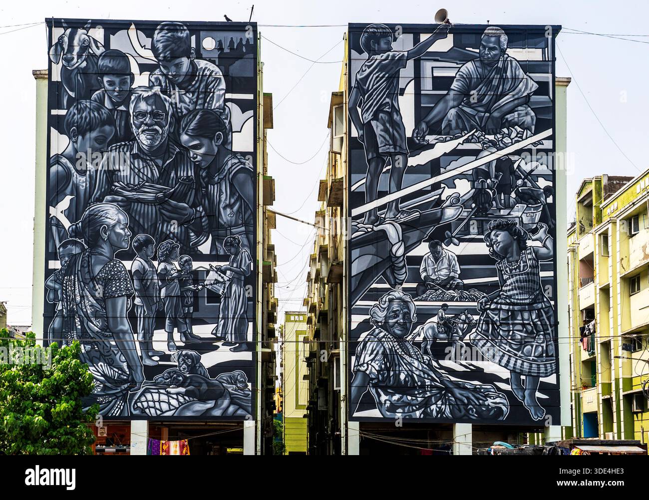 Deux grandes peintures murales sur des bâtiments adjacents représentant la vie communautaire en niveaux de gris. Banque D'Images