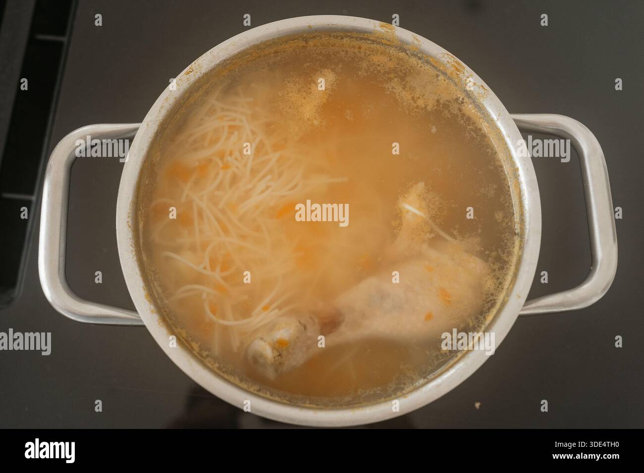 Une casserole de soupe au poulet mijotant sur la cuisinière avec des nouilles et des légumes visibles dans le bouillon. Le plat chaud et fait maison transmet le confort, la cuisine maison Banque D'Images