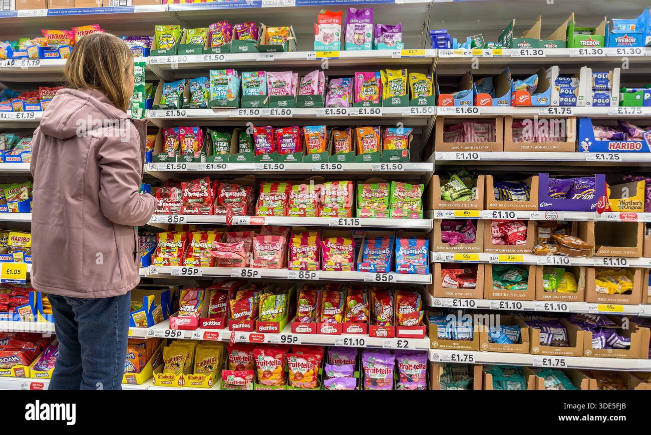 cliente femme parcourant une allée de supermarché tesco remplie de sucreries emballées assorties et de confiseries sur les étagères du magasin Banque D'Images