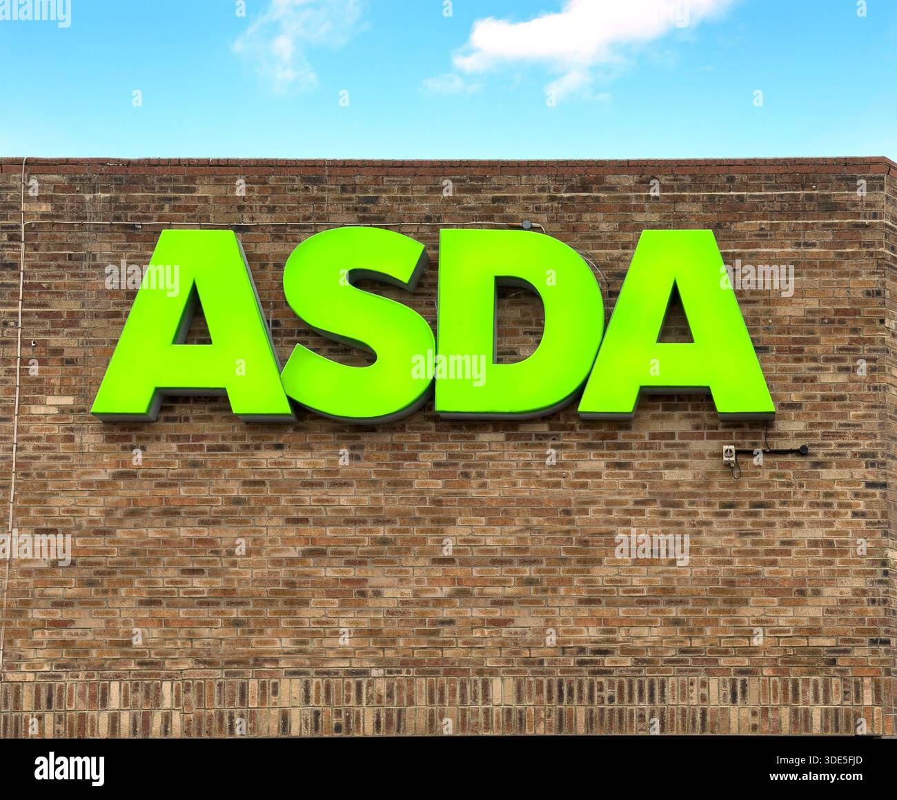Signe ASDA vert vif sur un mur de briques brunes représentant un extérieur de chaîne de supermarchés basé au Royaume-Uni contre un ciel clair Banque D'Images