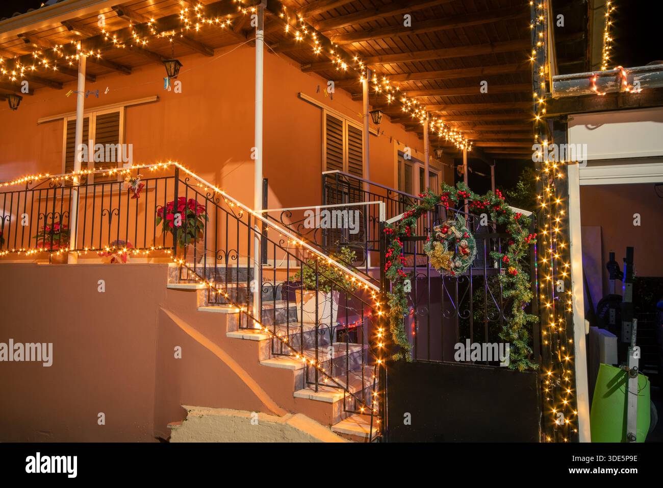 Extérieur de la maison de village grec traditionnel avec lumières de Noël festives, couronne et décorations poinsettia sur les escaliers et porte la nuit à Corfou Banque D'Images