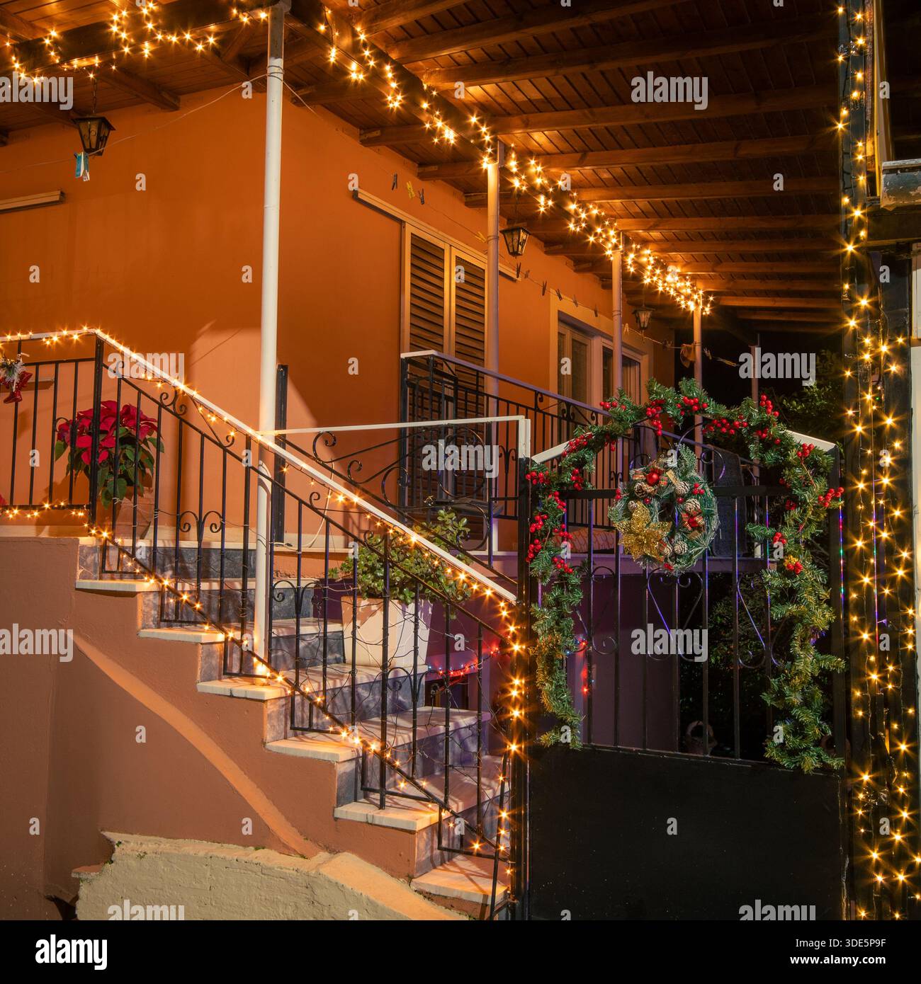 Extérieur de la maison de village grec traditionnel avec lumières de Noël festives, couronne et décorations poinsettia sur les escaliers et porte la nuit à Corfou Banque D'Images