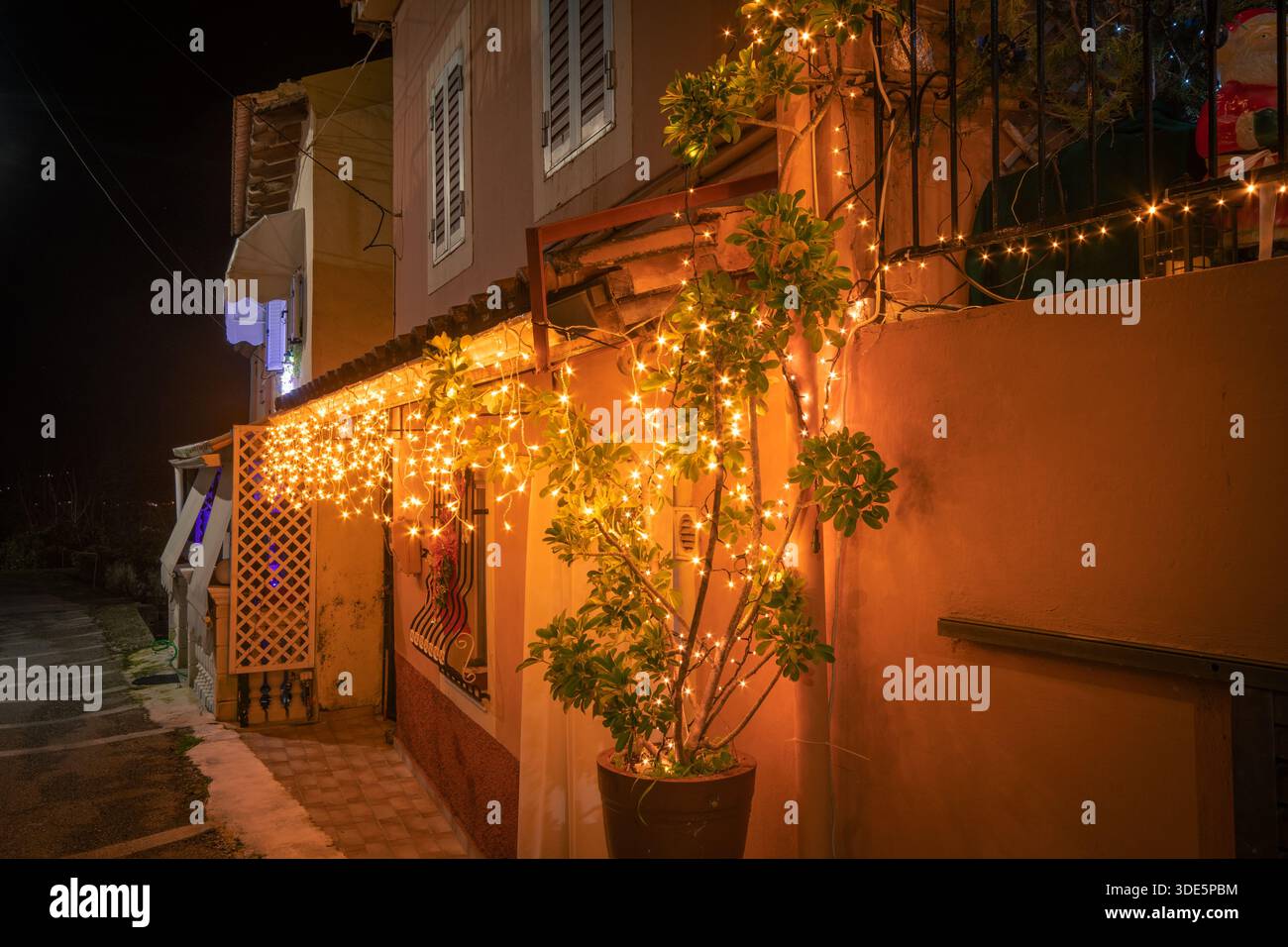 Scène festive de nuit de Noël dans un village grec avec arbre illuminé, lumières à cordes et décor de vacances sur une façade de maison traditionnelle à Corfou Banque D'Images