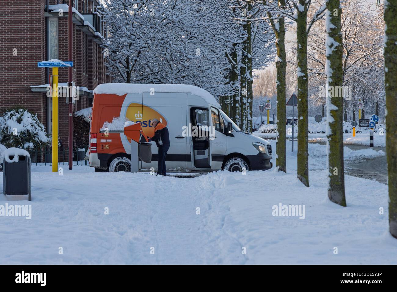 Camionnette de livraison PostNL et travailleur postal collectant le courrier dans une boîte aux lettres dans une rue résidentielle enneigée aux pays-Bas pendant l'hiver. Banque D'Images