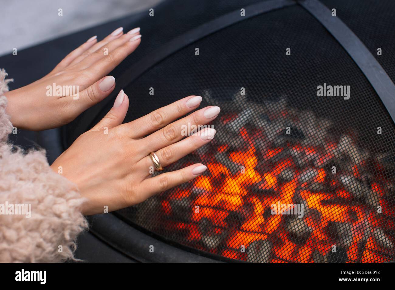 Femme se prélasser mains sur bol pour cheminée avec des charbons chauds à l'extérieur, gros plan. Banque D'Images