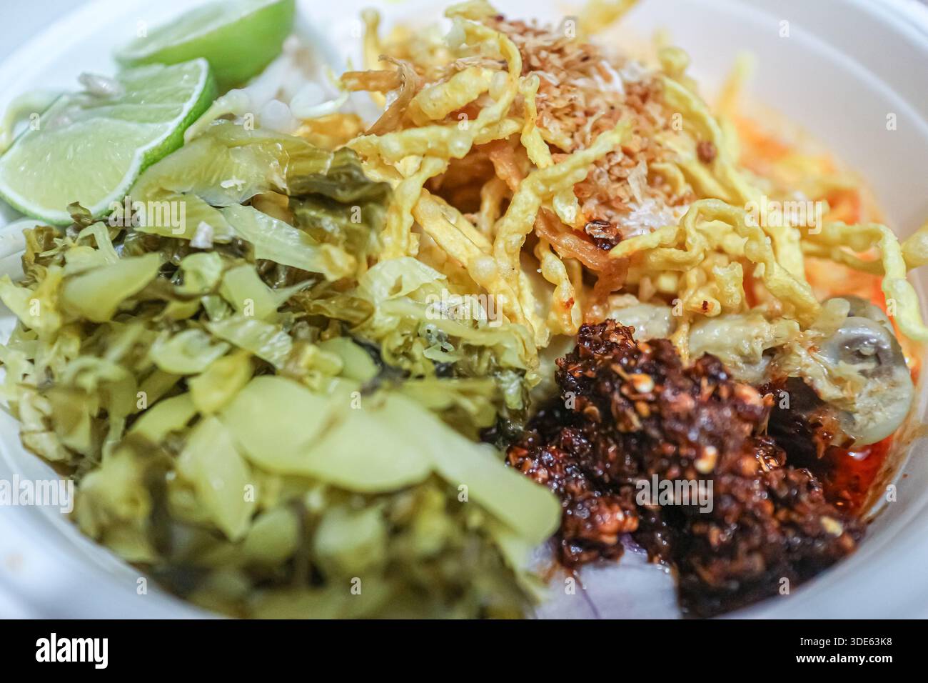 Gros plan sur les nouilles au curry de noix de coco du nord de la Thaïlande khao soi avec nouilles aux œufs croustillantes et garnitures traditionnelles, mettant en valeur une cuisine régionale authentique. Banque D'Images