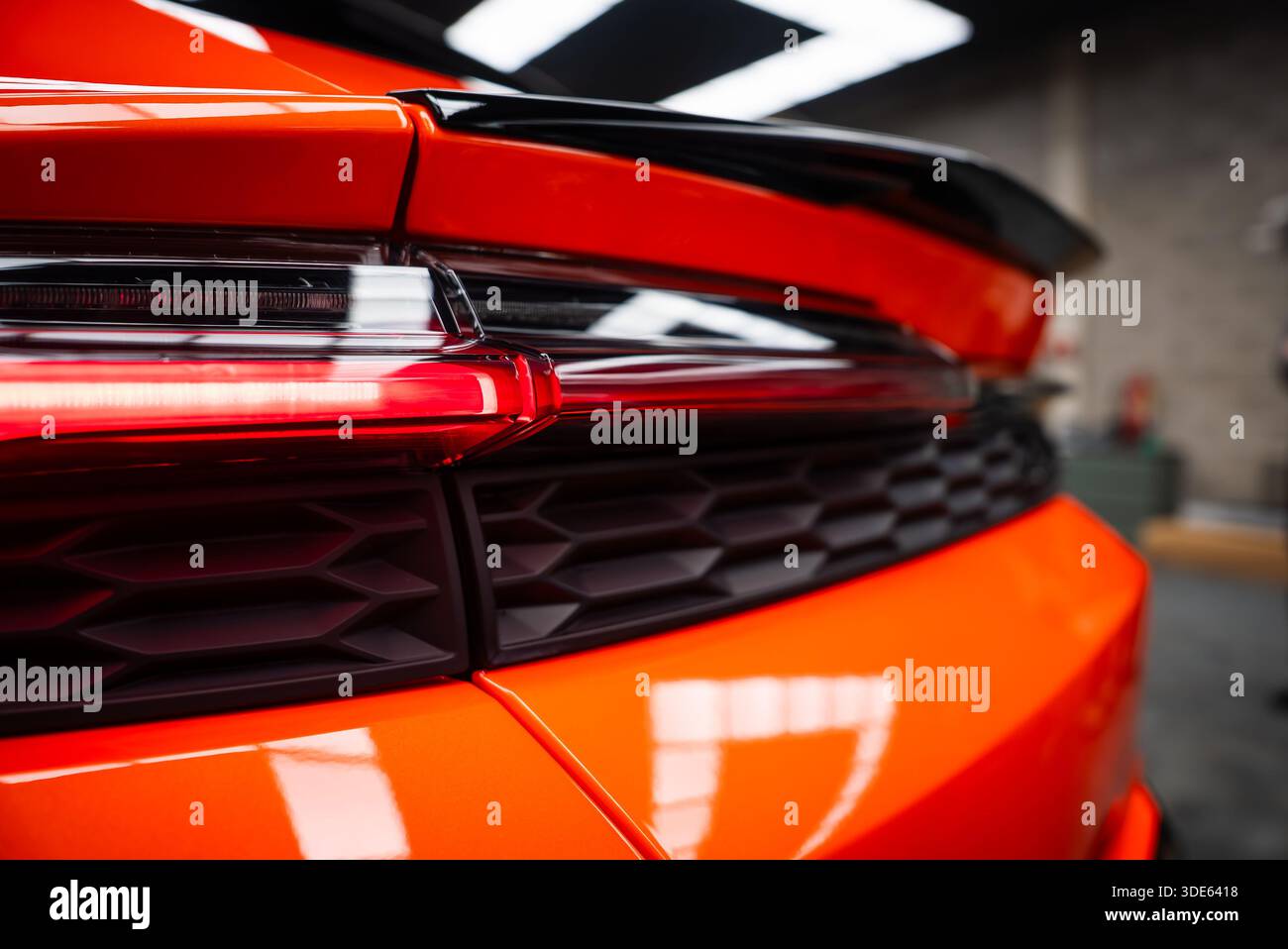 Vue rapprochée d'une Lamborghini Urus se orange dans un atelier, mettant l'accent sur le feu arrière, l'évent en nid d'abeille noir et le spoiler sculpté avec plafonniers refl Banque D'Images