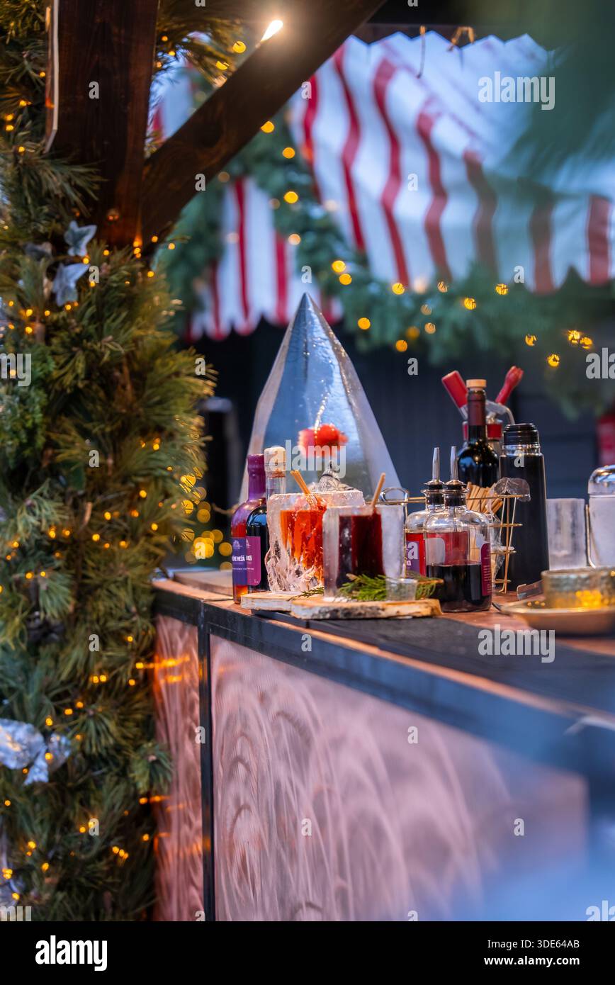 Un stand festif à Riga, Lettonie montre du vin chaud, des sirops et des épices à côté d'un cône de glace, sous un auvent rouge et blanc avec des guirlandes et une corde chaude L. Banque D'Images