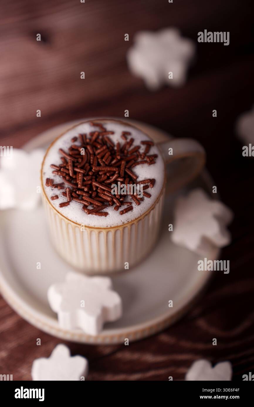 ambiance chaleureuse et accueillante avec une tasse de cappuccino mousseux garni de chocolat, entourée de guimauves en forme de flocon de neige sur une céramique Banque D'Images