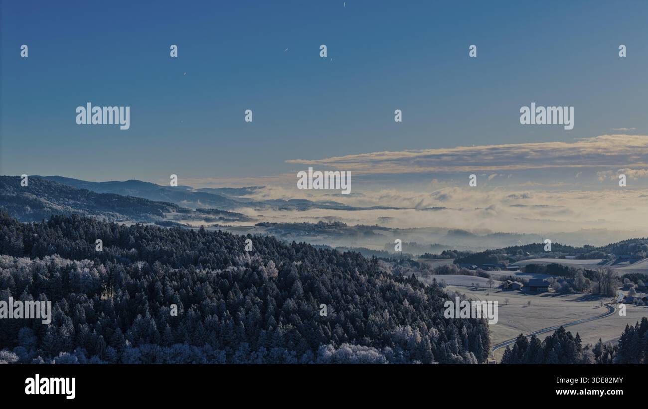 Le paysage hivernal montre des collines et des forêts. Le ciel est bleu et le soleil se lève. Il y a du brouillard sur la vallée et le froid peut être ressenti. Windberg, Banque D'Images
