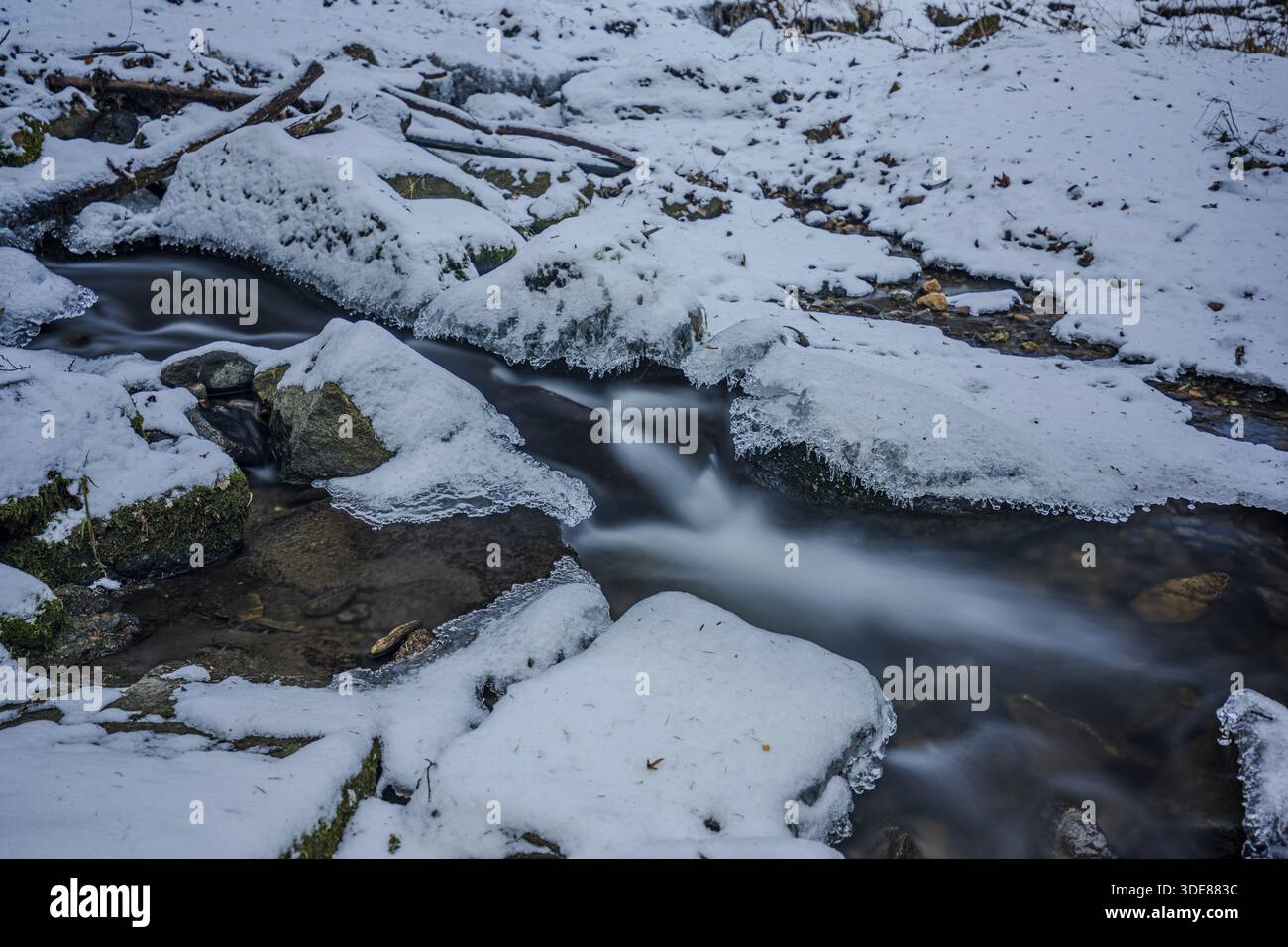 Un ruisseau coule à travers une zone de neige. Quelques pierres sont visibles et l'eau semble claire et fraîche. La région environnante est hivernale et calme. Perlba Banque D'Images
