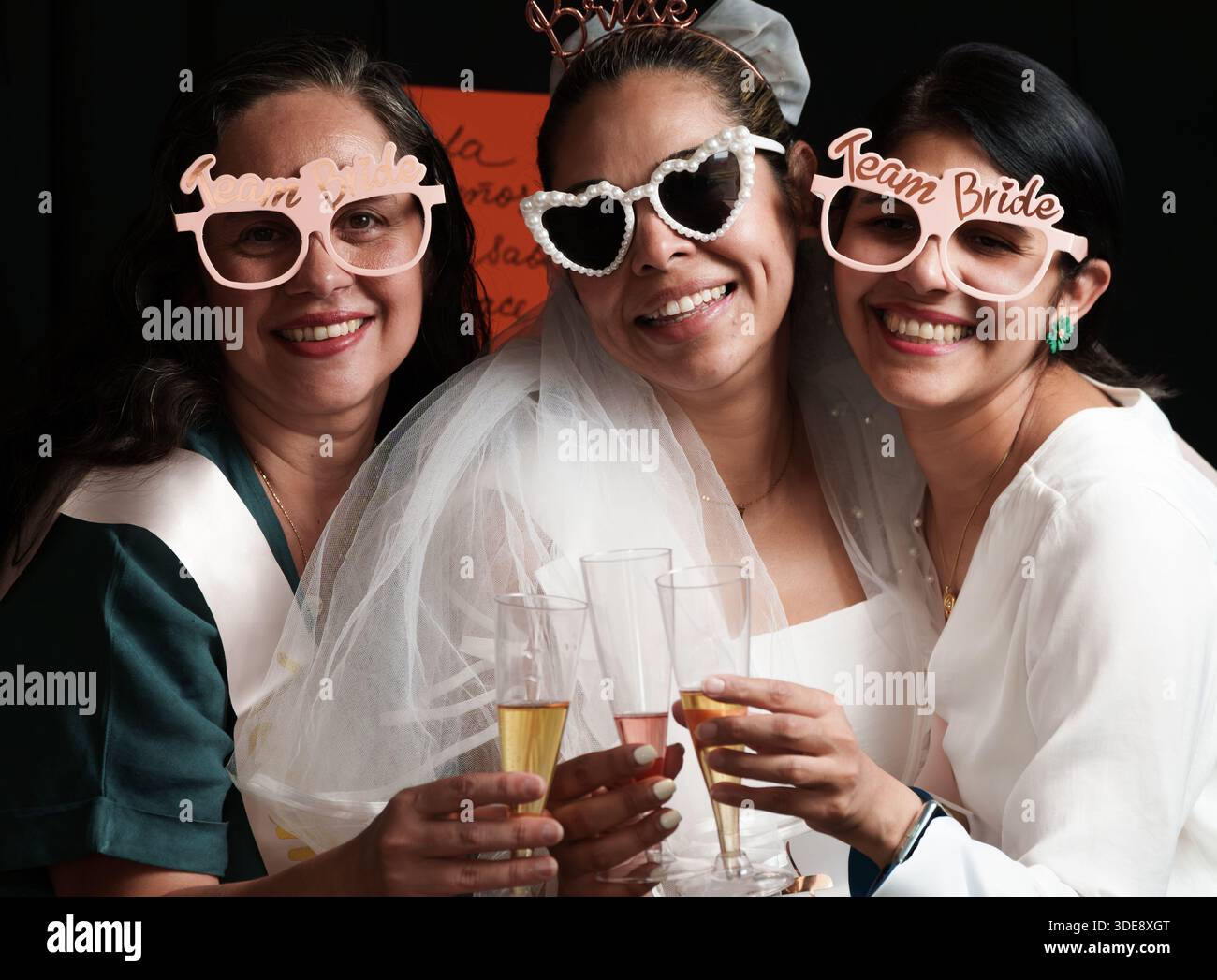 Trois femmes portent des lunettes de soleil et tiennent des verres de champagne. L'une des femmes porte une robe de mariée Banque D'Images