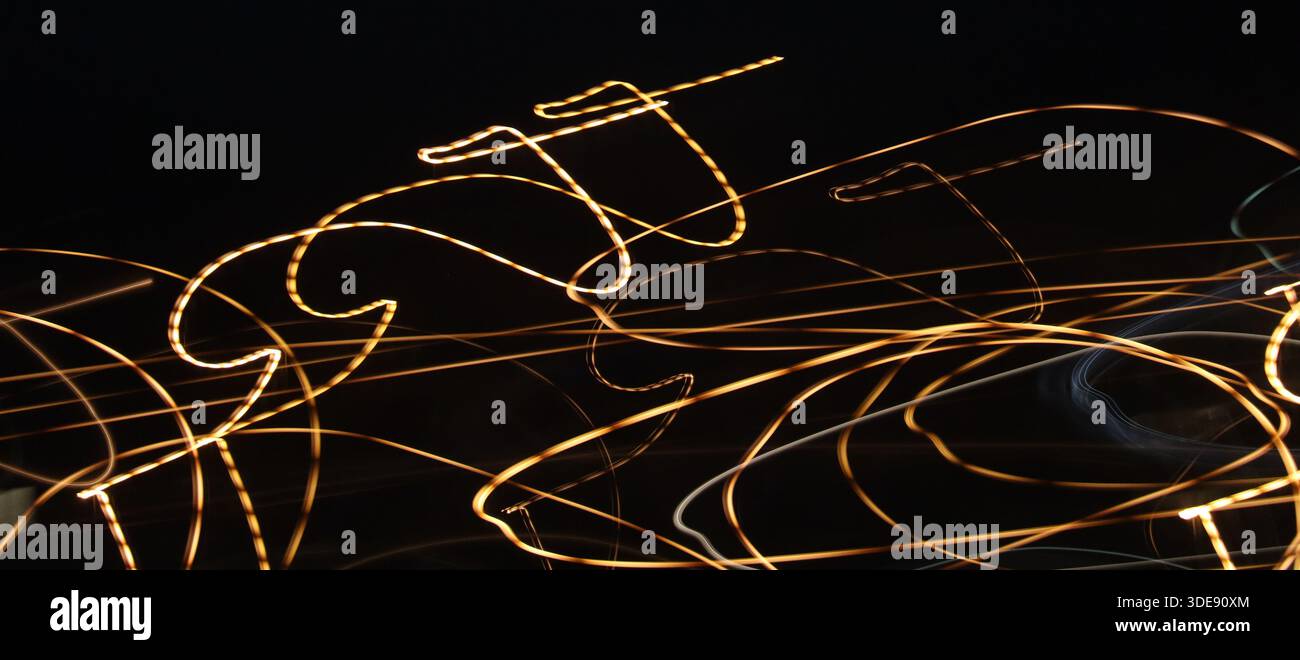 Peinture lumineuse énergique et chaotique avec des griffonnages au néon dorés et blancs éclatants. Ce cliché expérimental à longue exposition capture une dynamique. Banque D'Images