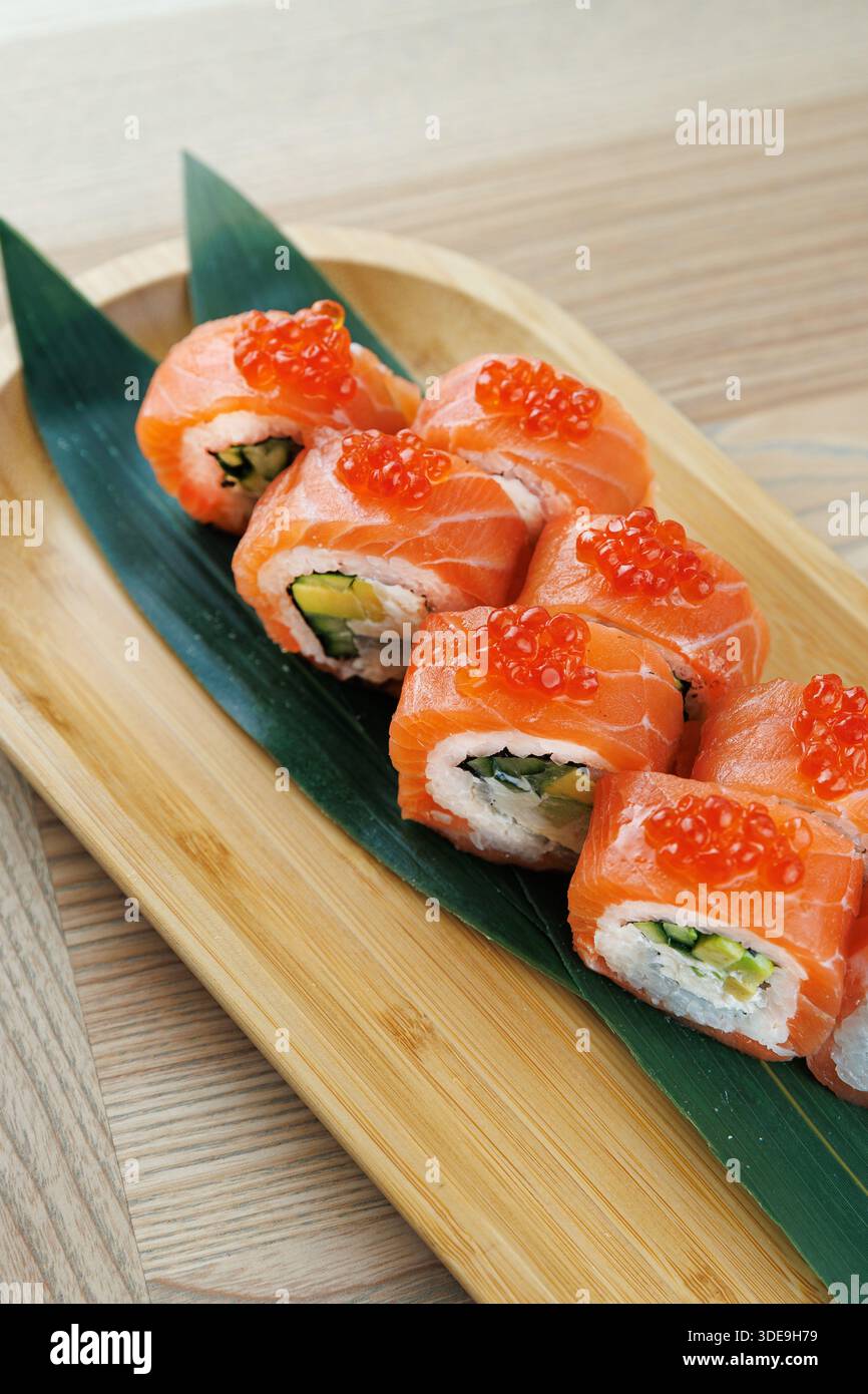 Les rouleaux de sushi lumineux sont soigneusement disposés sur un plateau en bois. Ces rouleaux comportent du saumon, de l'avocat et des garnitures, soulignant les couleurs vibrantes du Banque D'Images