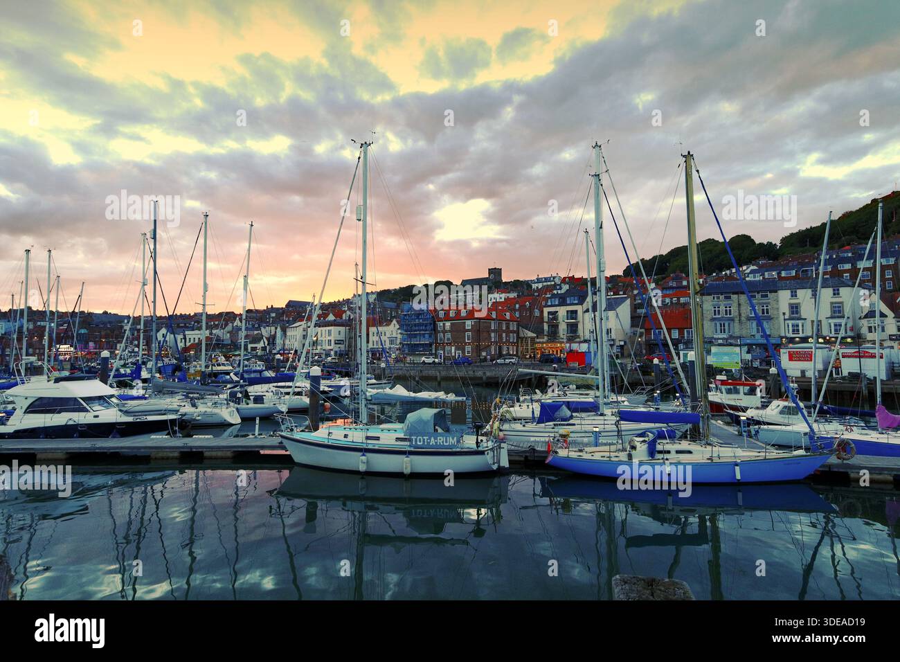 Yachts amarrés dans le port de Scarborough au coucher du soleil, avec le front de mer de la ville formant une toile de fond pittoresque sous un ciel nocturne spectaculaire - Yorkshire, Royaume-Uni Banque D'Images