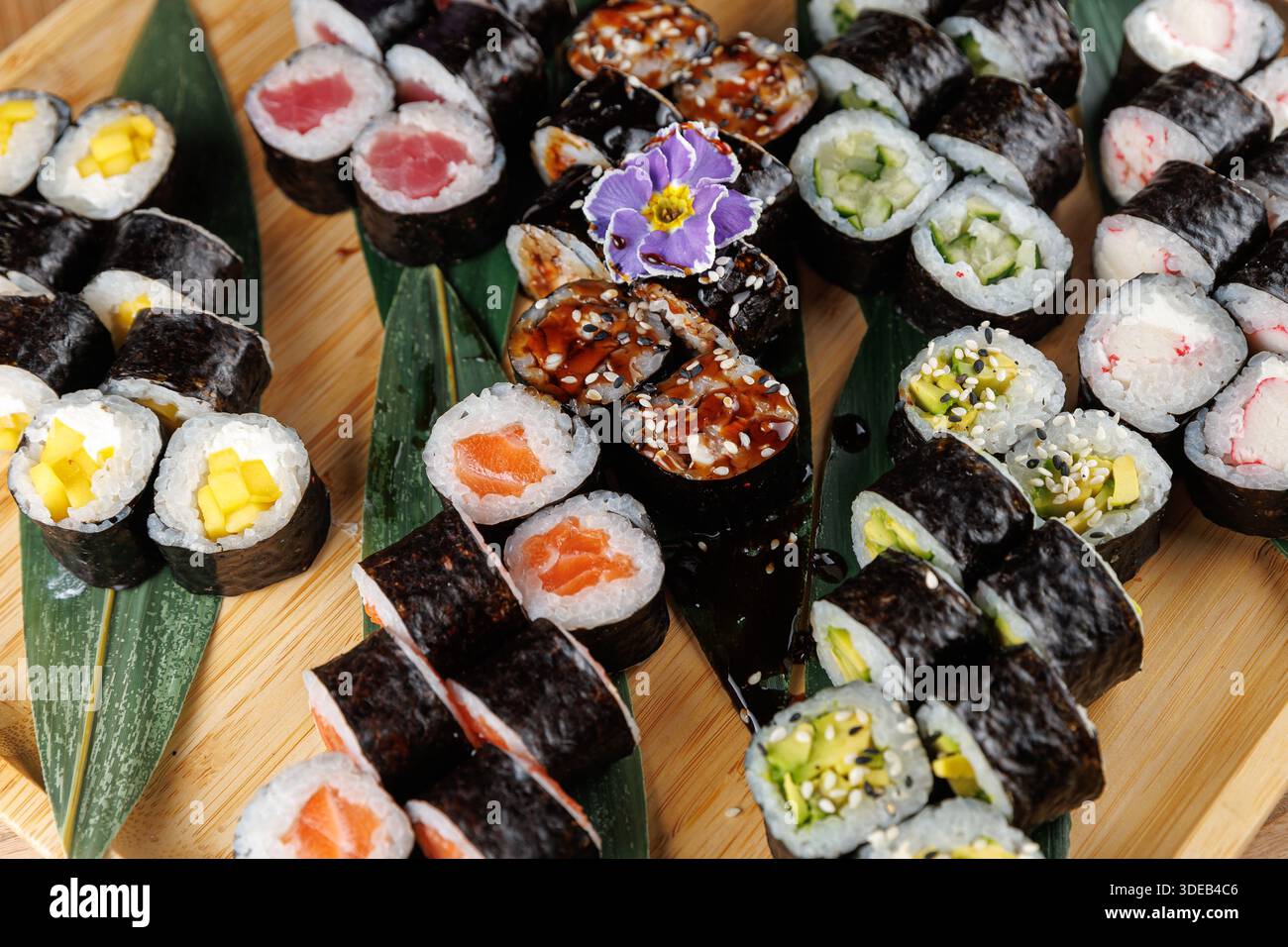 Divers rouleaux de sushi sont disposés sur un plateau en bois avec des feuilles vertes. Les rouleaux comprennent diverses garnitures et garnitures, mettant en valeur la cuisine japonaise Banque D'Images