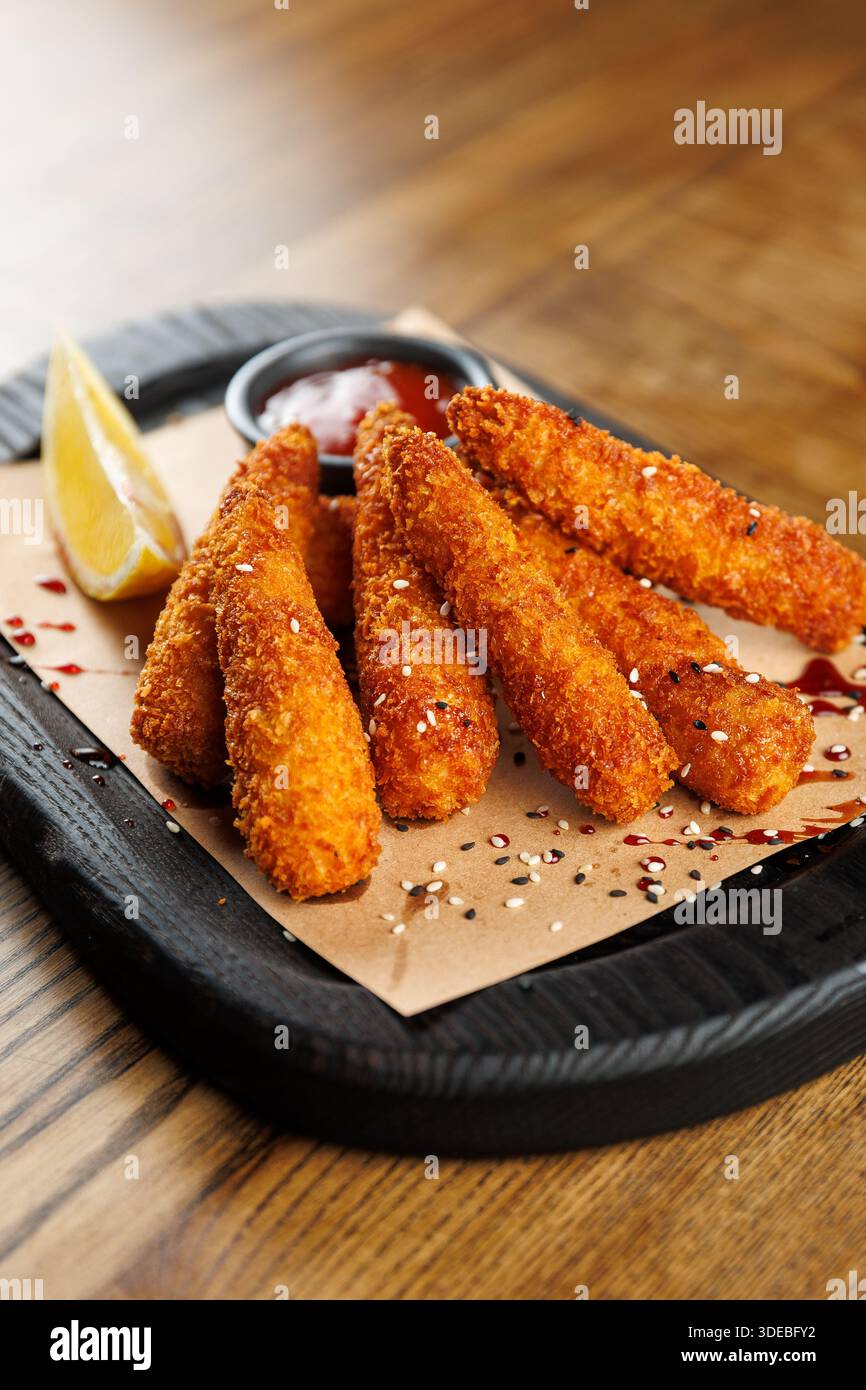 Les bâtonnets frits sont disposés sur un plateau en bois avec une tranche de citron et une sauce à tremper. Ce plat est apprécié dans une ambiance décontractée, parfait pour s Banque D'Images