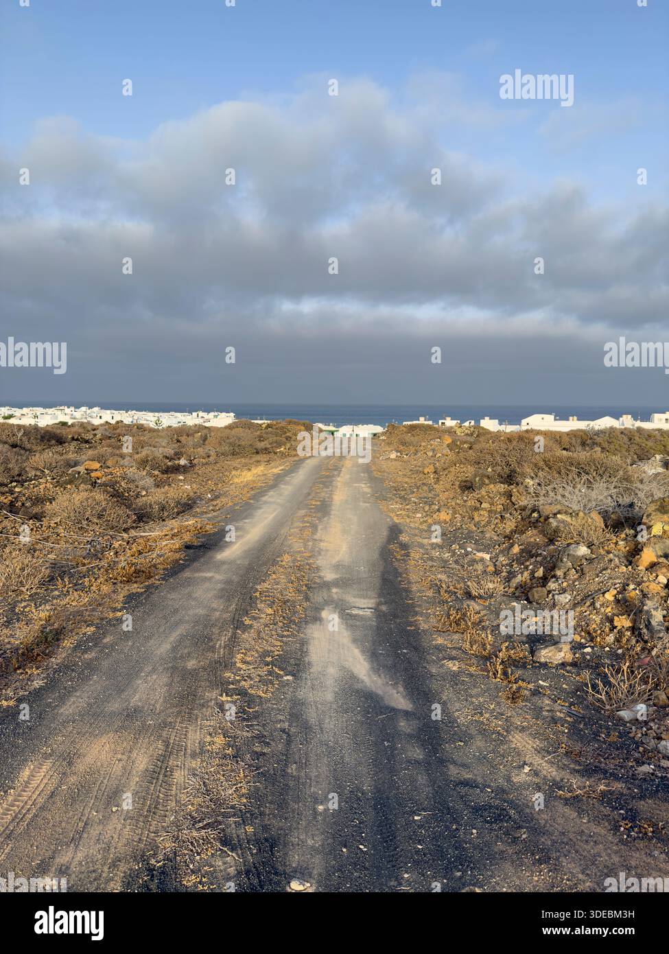 Un chemin de terre menant vers l'océan sous un ciel nuageux.. Lanzarote, Îles Canaries, Espagne, nuages Banque D'Images