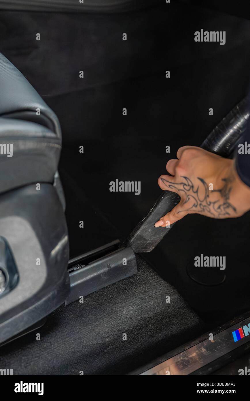 L'intérieur de la voiture en gros plan montre une main tatouée aspirant à côté des rails de selle, le seuil de porte tricolore BMW M visible, l'éclairage doux et uniforme et la faible profondeur de fie Banque D'Images