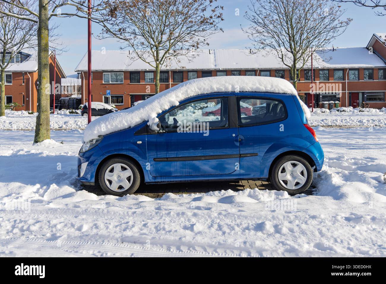 Voiture compacte bleue garée sur une rue résidentielle enneigée en hiver, couverte de neige fraîche, montrant le temps froid, la vie urbaine et les conditions saisonnières. UT Banque D'Images