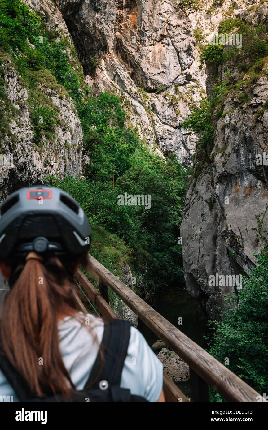 Une femme portant un casque regarde sur un chemin étroit. Le chemin est entouré d'arbres et de rochers Banque D'Images