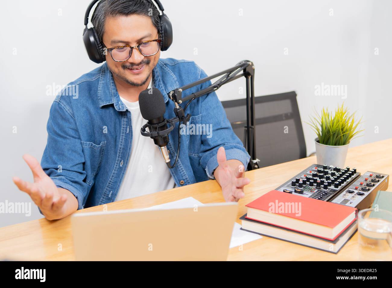 Homme barbu dans des écouteurs appréciant le podcasting dans son home studio. Beau podcaster riant tout en diffusant un podcast audio en direct Banque D'Images