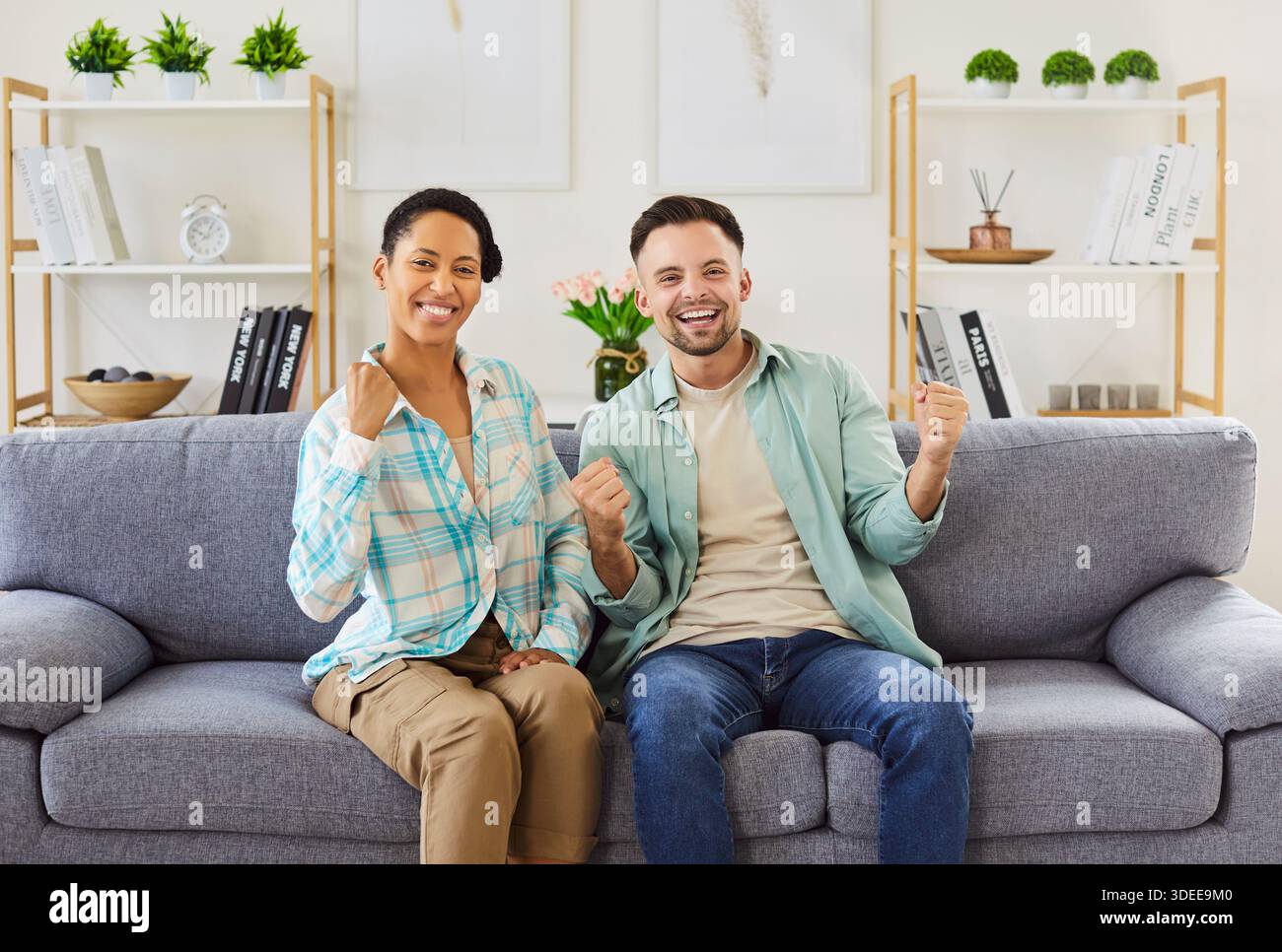 Joyeux couple biracial assis sur le canapé, regardant le sport à la télévision et célébrant la victoire Banque D'Images