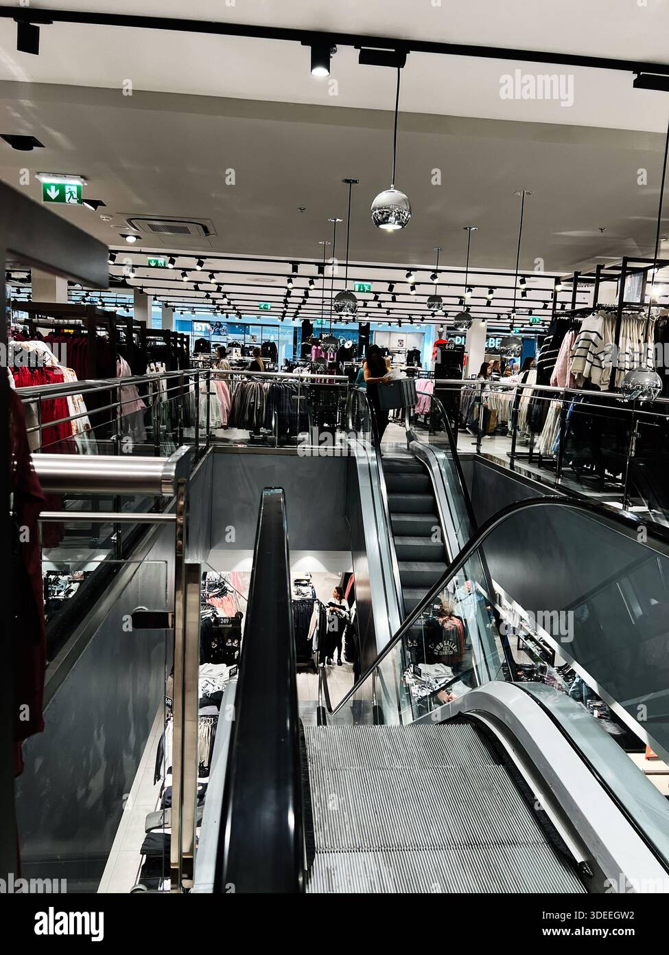 Brno, République Tchèque - 29 novembre 2025 : scène animée du centre commercial Galerie Vankovka avec escaliers mécaniques, rails de verre et porte-vêtements animés par les acheteurs. Banque D'Images