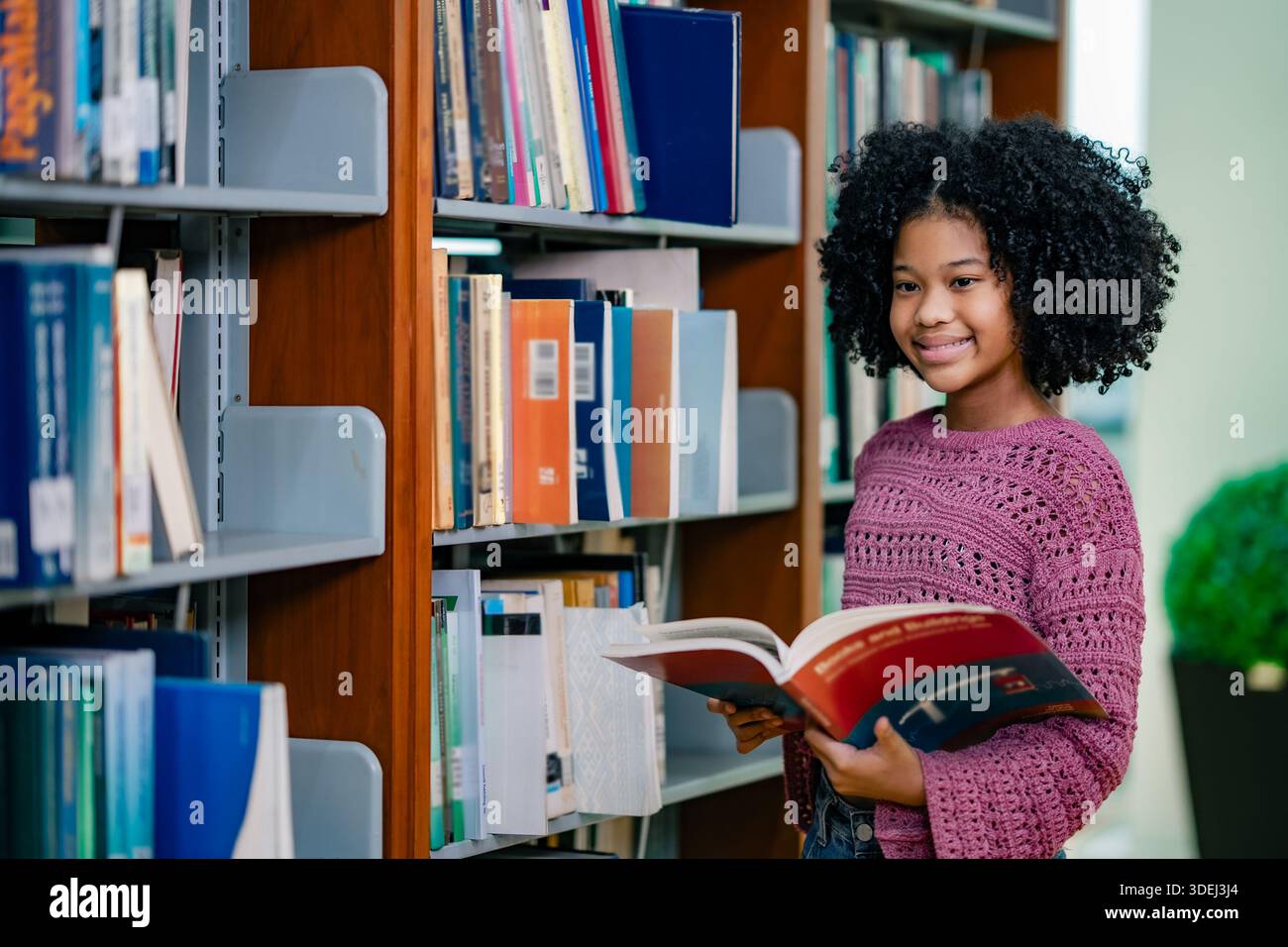 Étudiant tenant un livre tout en étudiant près des étagères de la bibliothèque. Une atmosphère calme communique la mise au point routine d'alphabétisation auto-apprentissage expérience positive en éducation Banque D'Images